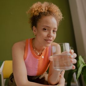 Frau in pink-orangem Top hält ein Glas Wasser Frau in pink-orangem Top hält ein Glas BRITA gefiltertes Wasser