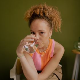 Eine Frau in pink-orangem Top trinkt aus einem ein Glas Wasser