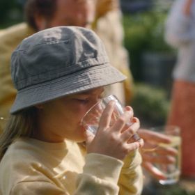 Ein Mädchen mit grauem Hut trinkt Wasser aus einem Glas Ein Mädchen mit grauem Hut trinkt Wasser aus einem Glas