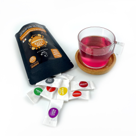 Umgekippte Teaballs Black Selection Verpackung GeöffneteTeaballs Black Selection Verpackung mit einzelnen Sachets neben einer gefüllten Teetasse.