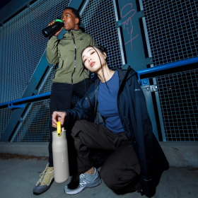 Zwei stylische junge Menschen posieren mit BRITA LARQ Flaschen, die ein farbiges Griffband haben. 