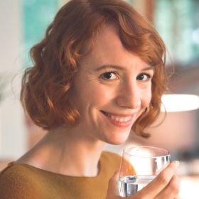 Frau lächelt mit Glas in Hand Frau lächelt mit einem Glas Wasser in der Hand.
