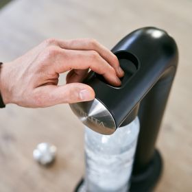Eine Hand drückt auf den Knopf am BRITA sodaONE.  Eine Hand drückt auf den Knopf zum Sprudeln am schwarzen BRITA sodaONE