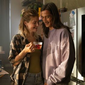 Ein lächendes Paar steht kuschelnd vor einer Küchentheke. Die Frau hat eine Tasse in der Hand. Ein lächelndes Paar mit einer Teetasse