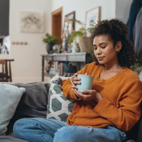 Junge Frau trinkt ein Heißgetränk auf dem Sofa Junge Frau chillt auf ihrer Couch mit einem Heißgetränk