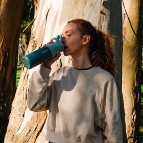 Frau trinkt aus einer grünen Wasserflasche im Freien.