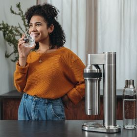 Frau trinkt ein Glas Wasser neben sodaTRIO pro. Eine Frau trinkt ein Glas Wasser neben dem sodaTRIO pro Wassersprudler.