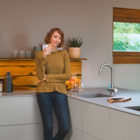 Frau steht neben BRITA 3 Wege Küchenarmatur mit einem Glas Wasser