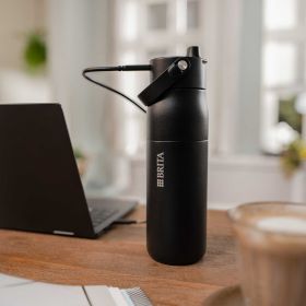 Eine schwarze BRITA LARQ iQ Filterflasche steht auf einem Schreibtisch im Homeoffice und wird per Kabel geladen – im Hintergrund ein Laptop und eine Kaffeetasse.