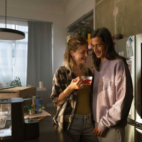 Ein lächendes Paar steht kuschelnd vor einer Küchentheke. Die Frau hat eine Tasse in der Hand.